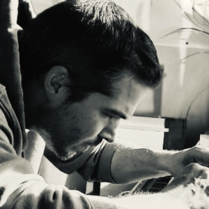 Black-and-white profile photo of Belgian guitar maker Colin Van Aelbrouck working at his bench in a hoodie