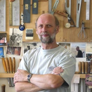 Guitar maker Simon Ambridge standing with arms crossed in front of a wall of hand tools in his workshop