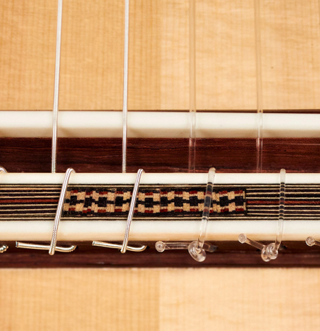 The bridge, saddle and nylon strings of a 2022 Mario Aracama classical guitar made of spruce and African rosewood