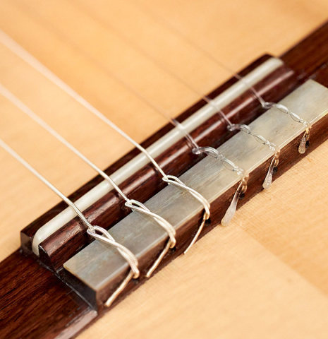 The bridge, tie-block and saddle of a 2019 Kevin Aram "Emily" classical guitar made of spruce and Indian rosewood