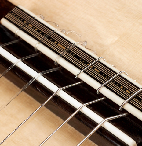 The bridge, saddle and nylon strings of a 2023 Mario Aracama classical guitar made of spruce and maple.