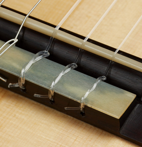 The bridge, tie-block and saddle of a 2021 Kevin Aram "Carmen 640" classical guitar made of spruce and Indian rosewood