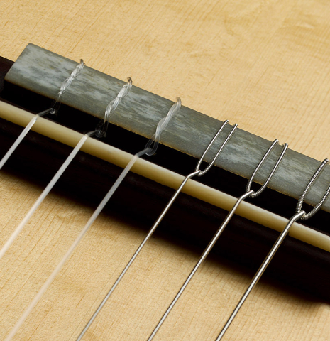 The bridge, tie-block and saddle of a 2021 Kevin Aram "Nancy" classical guitar made of spruce and satinwood