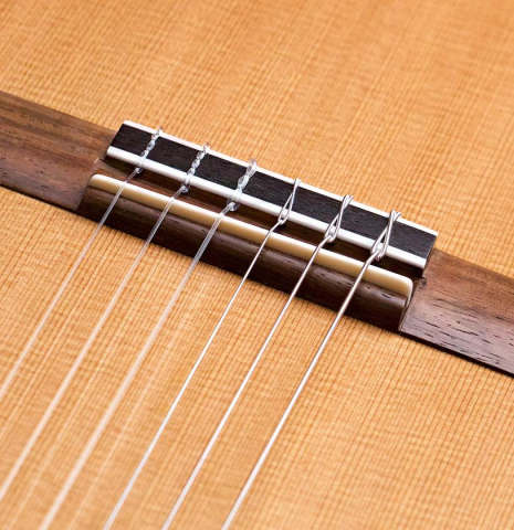 The bridge and nylon strings of a 2022 Asturias &quot;Double Top&quot; classical guitar made of cedar and Indian rosewood