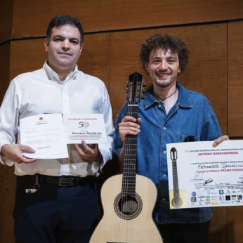 Vicente Coves and Francesco Baccaglion on stage, Francesco holding his prize-winning guitar and First Prize certificate