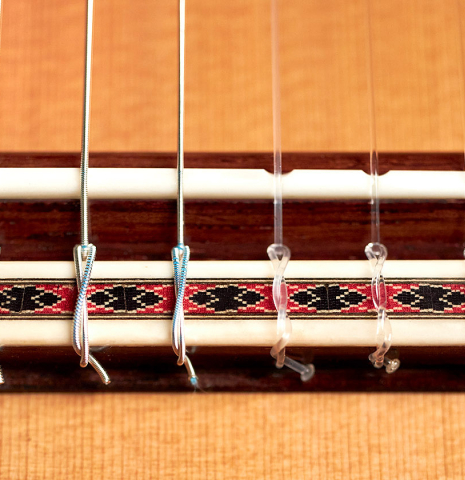 The bridge, saddle and nylon strings of a 2022 Michel Belair "Hommage a Daniel Friederich" classical guitar made of cedar and Indian rosewood
