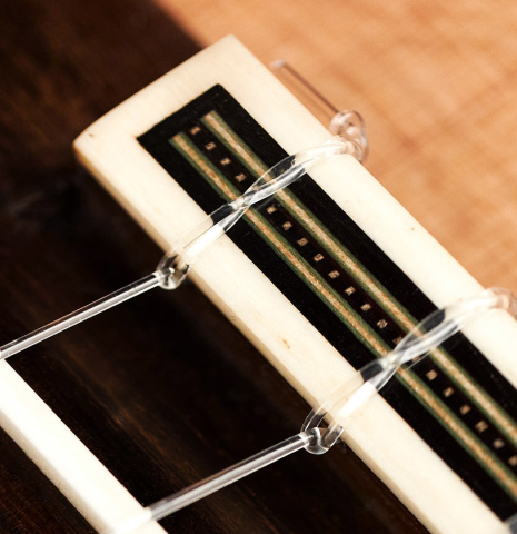 The tie-block and saddle of a 2023 Amélie Bouvret classical guitar made of cedar and figured mahogany.