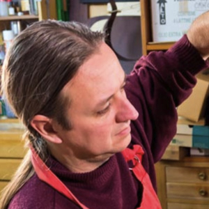 Guitar maker Ivan Bruna in a red apron and purple sweater working in his workshop