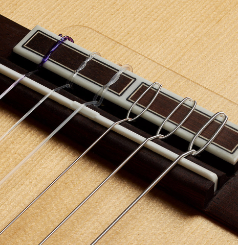 The bridge, tie-block and saddle of a 2024 Hermanos Camps "CL20-S" classical guitar made of spruce and Malaysian blackwood