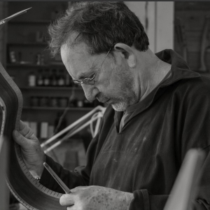Black-and-white photo of Brian Cohen in his workshop, studying a bent guitar side with its kerfed lining