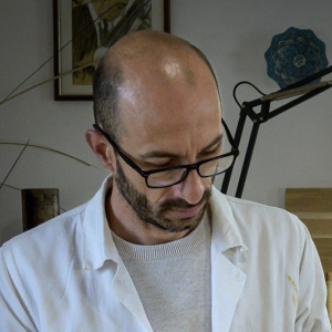 Thomas Dauge in a white workshop coat and glasses, looking down at his work