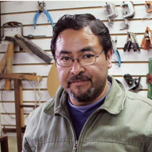 Abel García in a green jacket in his workshop, with tools hanging on the wall behind him