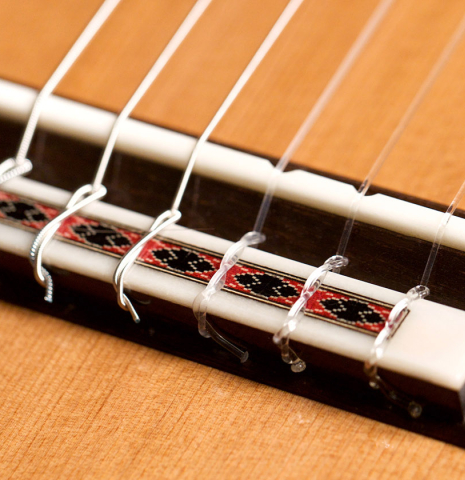 The bridge and nylon strings of a 2022 Michel Belair &quot;Hommage a Daniel Friederich&quot; classical guitar made of cedar and Indian rosewood