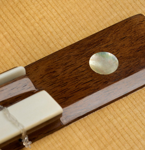 The wings of the bridge with mother-of-pearl inlay of a 2025 Yulong Guo "Torres SE 124" classical guitar made of spruce and Indian rosewood