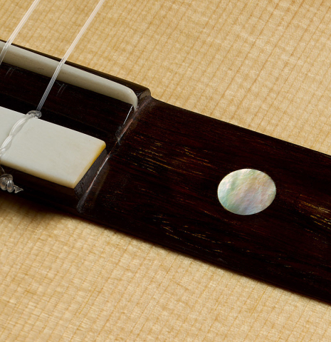 The wing of the bridge with mother-of-pearl inlay of a 2025 Yulong Guo "Torres SE 124" classical guitar made of spruce and cypress