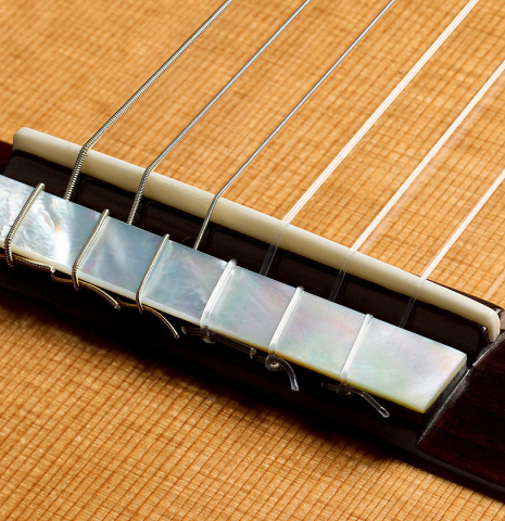 The bridge, tie-block and saddle of a 2025 Kenny Hill "New Century CD/SP" classical guitar made of a cedar/spruce double-top and Indian rosewood back and sides