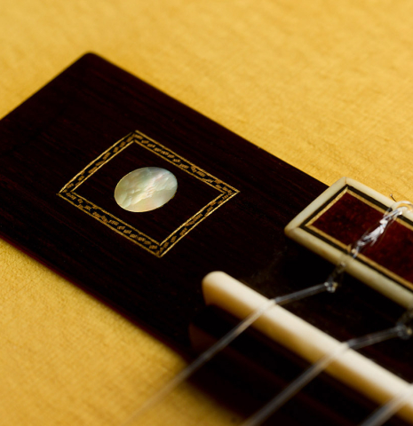 The wing of the bridge with mother-of-pearl inlay of a 2017 Richard Howell classical guitar made of spruce and maple