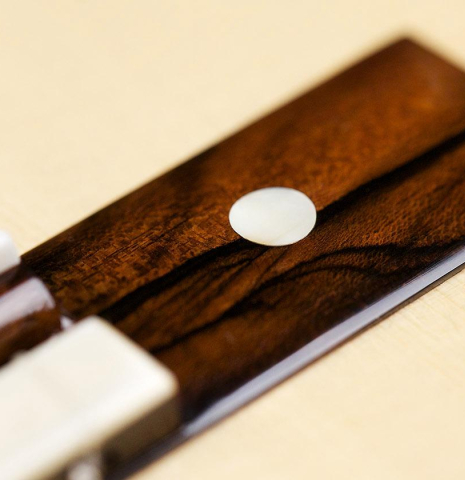 The close-up of a bridge and saddle of a La Cañada "Model 115" classical guitar made with spruce and granadillo