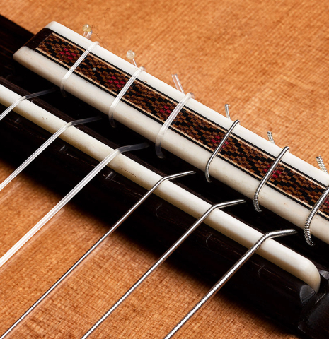 The bridge, tie-block and saddle of a 2024 Paula Lazzarini "Roma Guitar Expo" classical guitar made of cedar and cocobolo