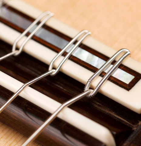 The bridge and saddle, and nylon strings of a 2021 Lucas Martin classical guitar made with spruce and Indian rosewood