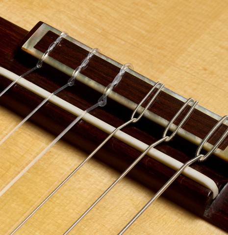 The bridge, tie-block and saddle of a 2021 Paco Santiago Marin "50th Anniversary" classical guitar made of spruce and Indian rosewood