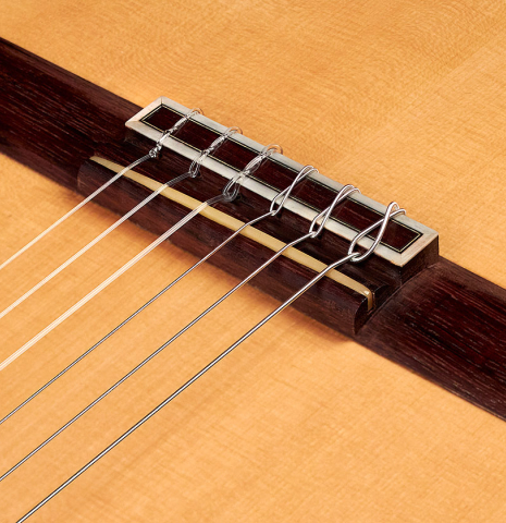 The bridge, saddle, and nylon strings of a 2013 Robert Mattingly "Posthumous" classical guitar made of spruce and Indian rosewood