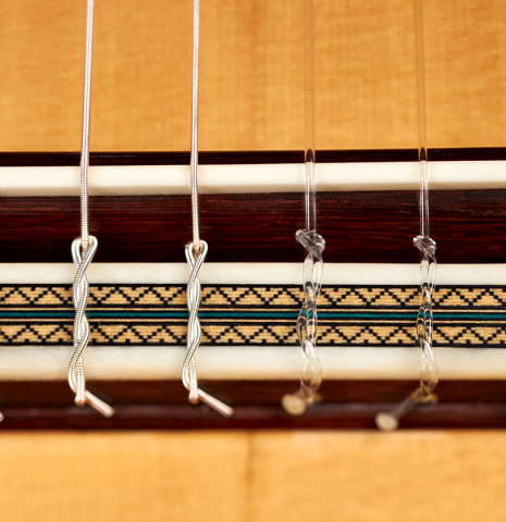 The ornamented bridge and nylon strings of a 2022 Teodoro Perez &quot;Especial&quot; classical guitar made of spruce and cocobolo