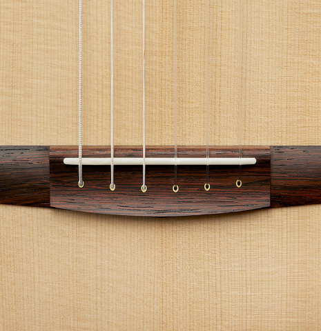 The bridge, tie-block and saddle of a 2024 Richard Reynoso w/pegs classical guitar made of spruce and Indian rosewood