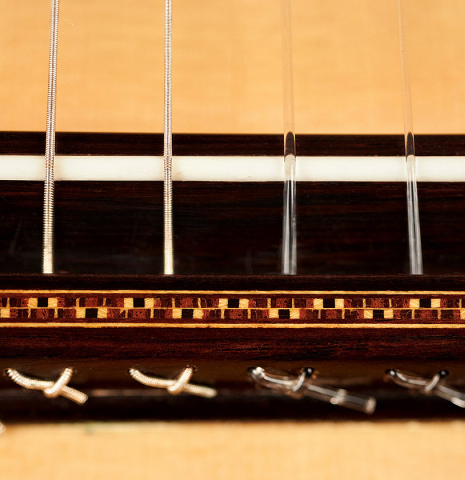 Detail of the bridge, tie-block and saddle of a 2017 Jose L. Romanillos &amp; Son "La Campanula Azul" classical guitar made with spruce and Indian rosewood.