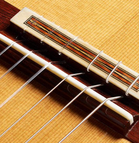 The bridge, tie-block and saddle of a 2023 Jean Rompre classical guitar made of cedar and Indian rosewood
