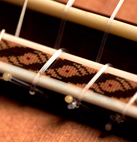 The ornamented bridge and saddle of a 2022 German Vazquez Rubio "Solista" classical guitar made with cedar and Indian rosewood The ornamented bridge and saddle of a 2022 German Vazquez Rubio "Solista" classical guitar made with cedar and Indian rosewood
