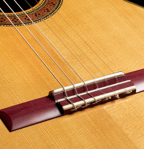 The bridge, tie-block and saddle of a 2023 German Vazquez Rubio "Classic Estudio" classical guitar made of spruce and Palo Escrito.