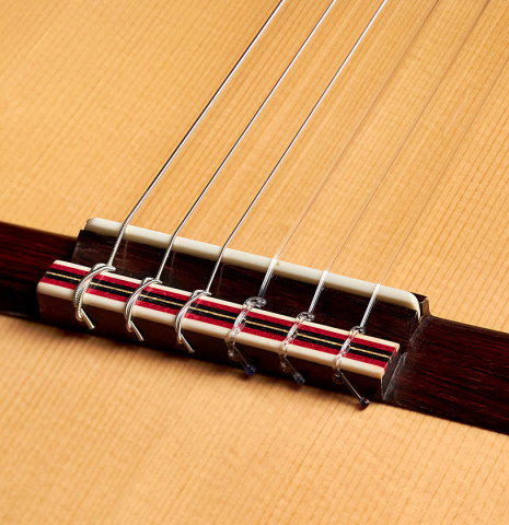 The bridge, saddle and strings of a 2001 Otto Vowinkel 640 scale classical guitar made of spruce and CSA rosewood