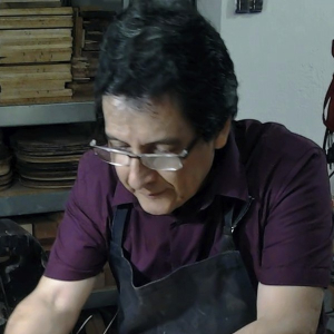 Fructuoso Zalapa in an apron at his workbench, gluing the binding of a classical guitar