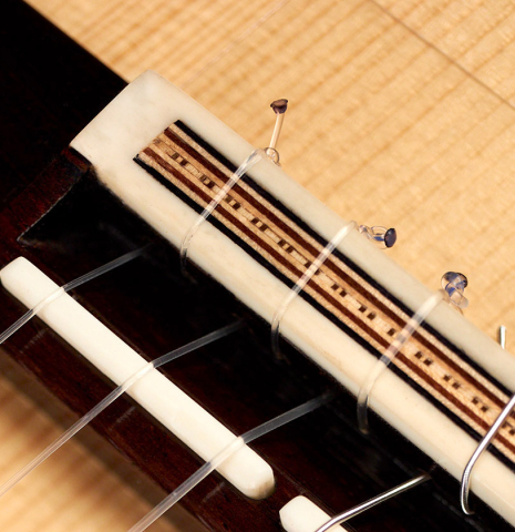The bridge, broken saddle, and tieblock of a 2022 Fructuoso Zalapa "Romanillos" classical guitar made of spruce and maple