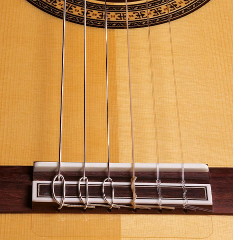 The bridge and nylon strings of a 2022 Hermanos Camps &quot;Primera Blanca&quot; flamenco guitar made of spruce and cypress