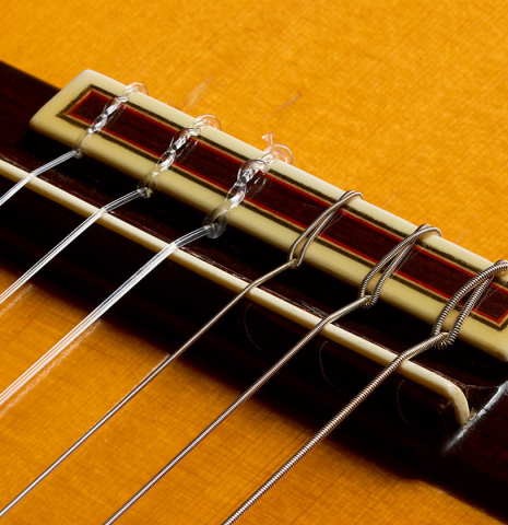 The bridge, tie-block and saddle of a 1992 Conde Hermanos w/pegs flamenco guitar made of spruce and cypress