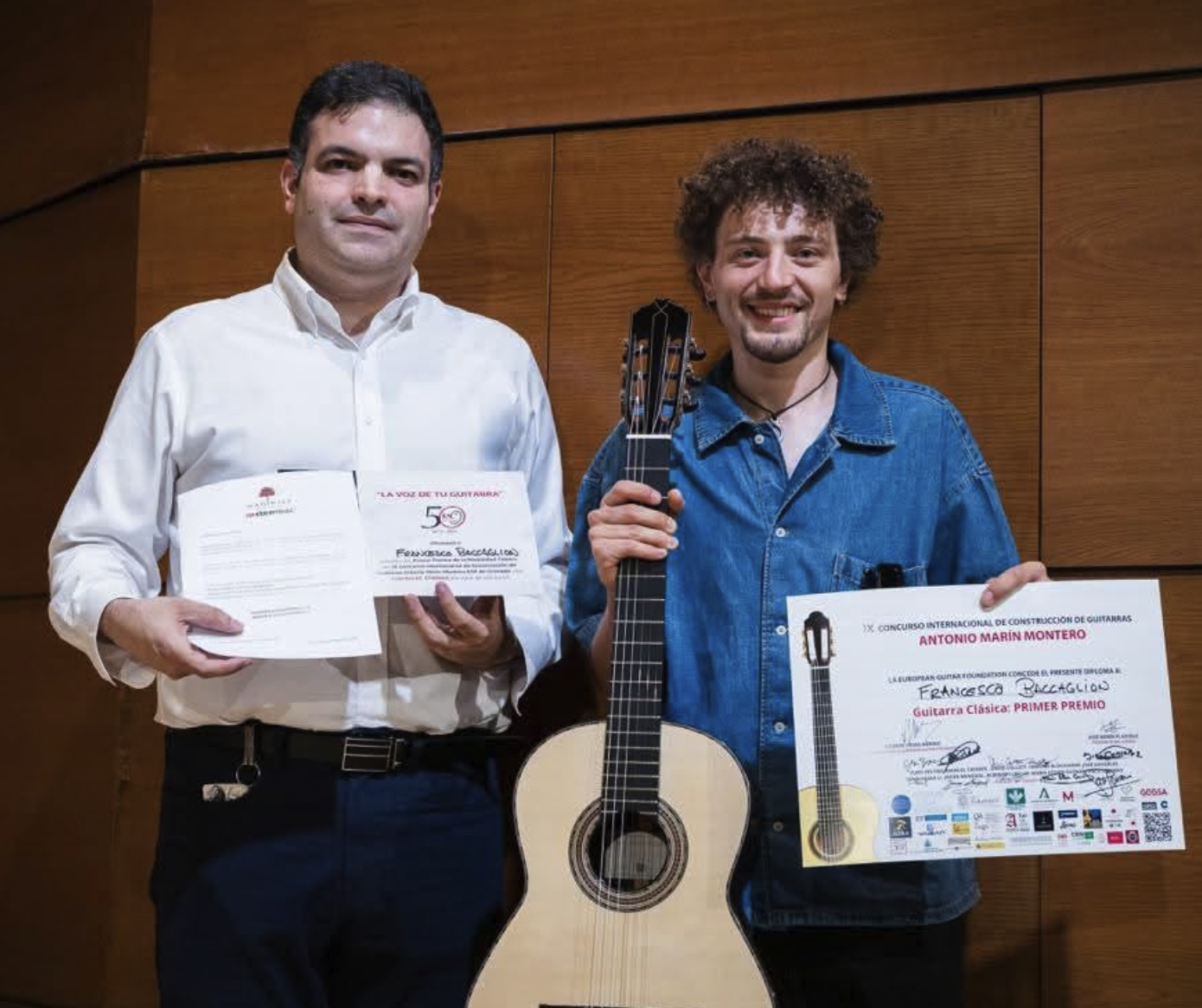 Vicente Coves and Francesco Baccaglion on stage, Francesco holding his prize-winning guitar and First Prize certificate